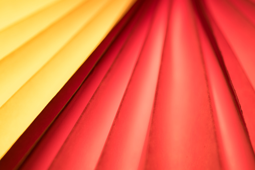 Close up of a yellow and red fluted paper fan.