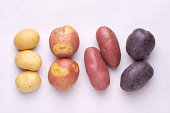 Different types of potatoes on white wooden background