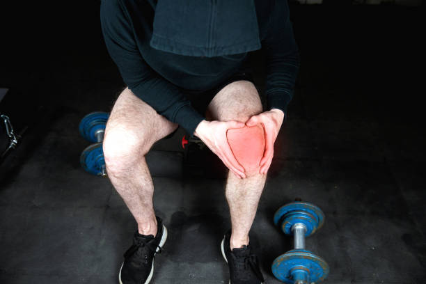 verticale d’un homme de forme physique de muscle atteignant pour son genou dans la douleur, blessure d’hommes de l’exercice dans le plan rapproché de gymnastique de la jambe avec le rouge entouré - foot massage photos et images de collection