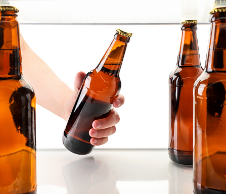 A man's hand takes out a bottle of beer from the refrigerator on a white background isolated. The view from the fridge