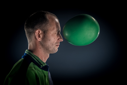 Side view of a man about to be hit by a green water balloon in mid-air.