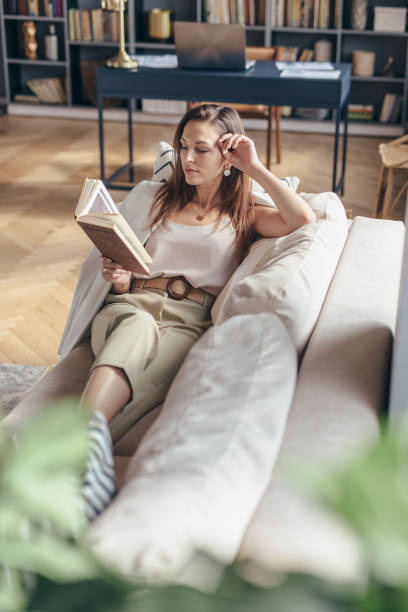 istock Young woman at home lying on couch and reading book. 1225430952