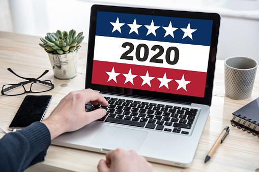 Online election, digital Voting on 2020 US America election. Man working with a computer laptop, 2020 on display, office background.