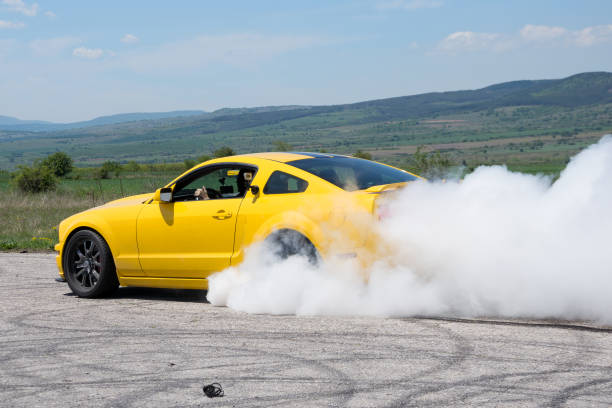 Sports car tires burnout Kraynitsi, Bulgaria - May 12, 2019: Yellow muscle car in smoke burning tires on a racetrack. Sunny summer day on the former Kraynitsi airport runway near Dupnitsa, Bulgaria car burnout stock pictures, royalty-free photos & images