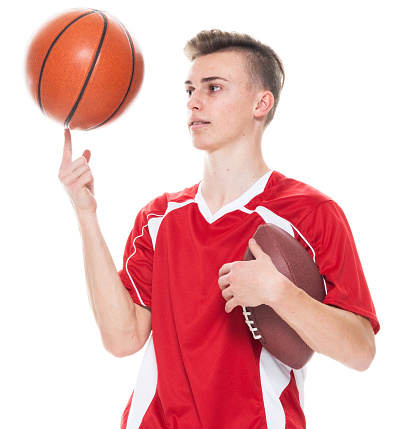 Front view of aged 16-17 years old caucasian young male american football player standing in front of white background wearing soccer uniform who is laughing and holding basketball - ball and playing soccer - sport and using sports ball