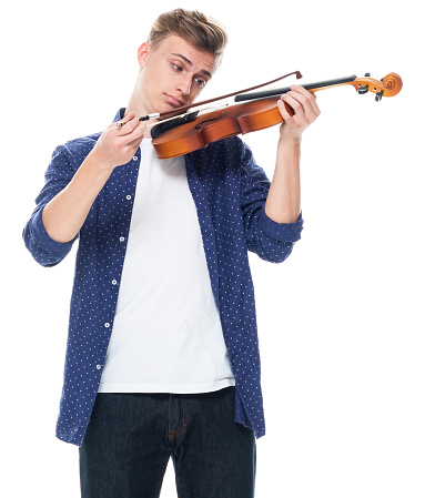 Portrait of aged 16-17 years old with brown hair caucasian male violinist standing in front of white background wearing pants who is happy and holding violin