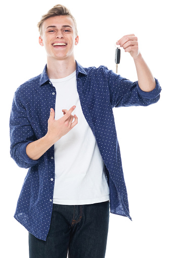 Portrait of aged 16-17 years old with brown hair caucasian male car salesperson standing in front of white background wearing shirt who is showing cool attitude and holding key ring