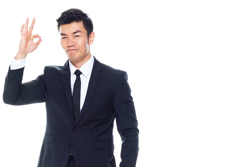 Waist up of aged 20-29 years old chinese ethnicity male standing in front of white background who is smiling and showing hand raised