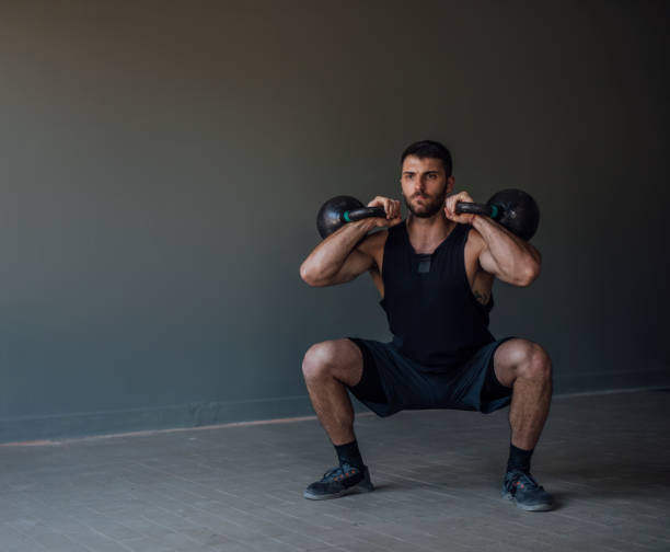 istock Strong Man in Sportswear Squatting while Holding Kettlebell Weights (Copy Space) 1225440109