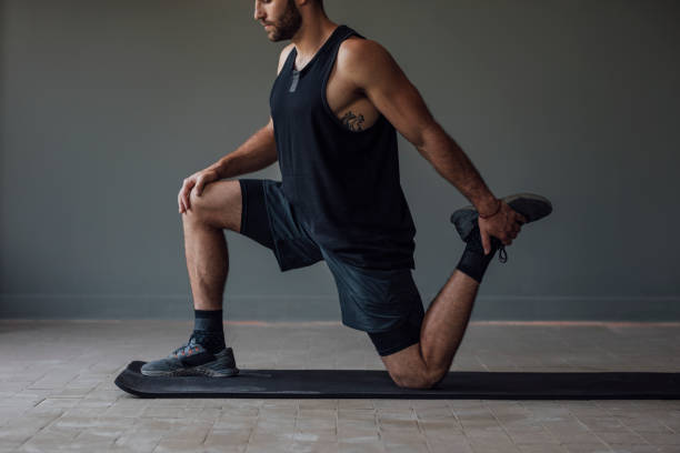 Muscular Sportsman Stretching his Legs to Warm Up for a Workout Training preparations: a strong athlete getting ready to exercise by stretching his legs. stretched leg stock pictures, royalty-free photos & images