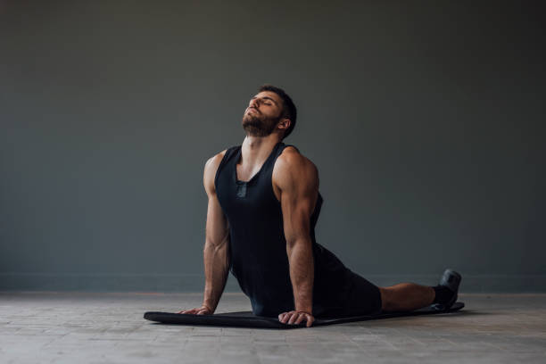 Handsome Muscular Athlete Doing Yoga Alone - Stretching in the Cobra Pose Man relaxing after a challenging workout by doing yoga. snakes beard stock pictures, royalty-free photos & images