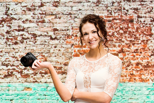 Waist up of aged 20-29 years old who is beautiful with curly hair caucasian female photography wearing dress who is cheerful who is photographing and holding camera