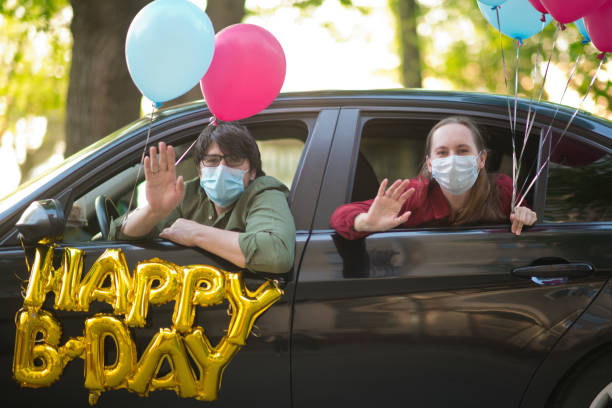 family wishing happy birthday to a friend or relative from their car during an infectious disease epidemic. they are keeping social distancing and wearing protective masks - illness mask pollution car imagens e fotografias de stock