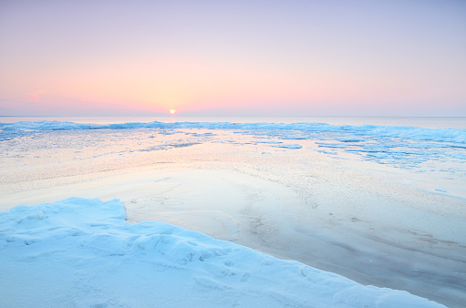 Panoramic view of the snow-covered shore of the frozen Saima lake at sunset. Ice fragments close-up. Colorful cloudscape. Symmetry reflections on the water. Finland