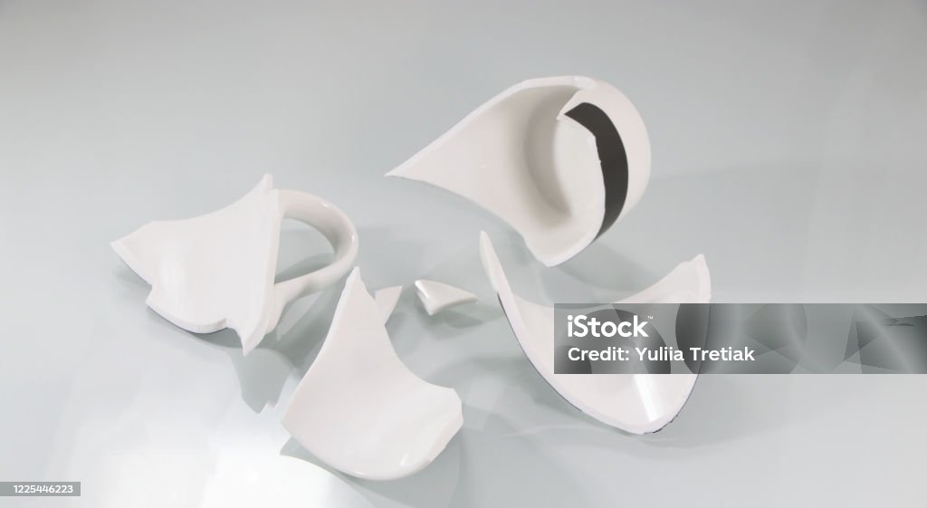 Broken white cup, on white. Broken white cup, on white. Shards of broken utensils. An empty bowl is broken into pieces. Broken Stock Photo