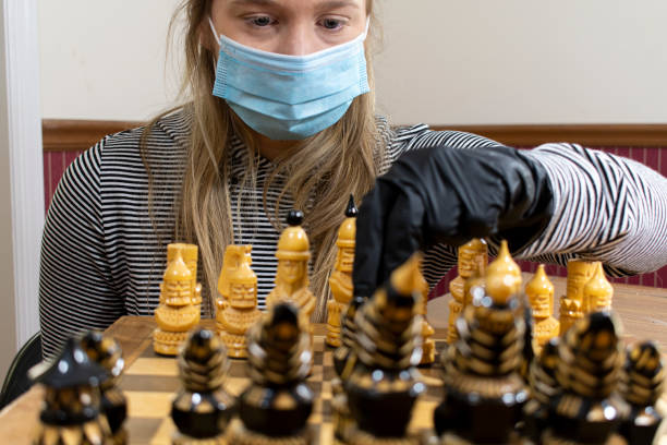 istock Young woman playing chess wearing protective mask and gloves 1225448376