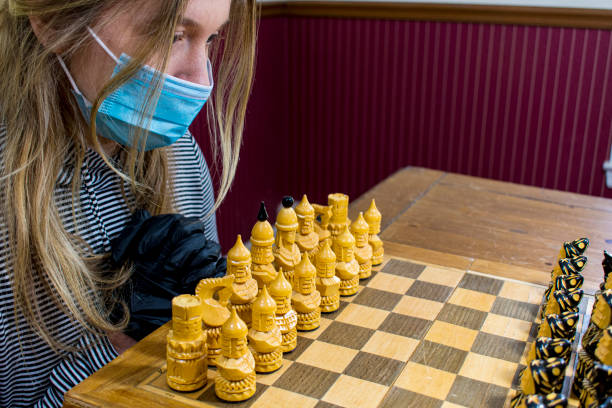 istock Young woman playing chess wearing protective mask and gloves 1225448380