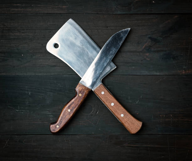 two sharp knives lie on a brown wooden surface, kitchen items are crossed