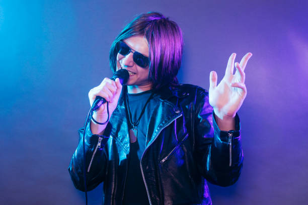 young rock star singing in microphone The young rock star in black leather is singing in microphone on blue purple background. emo boy stock pictures, royalty-free photos & images