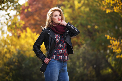 Young fashion blonde woman walking in city park  Stylish female model in black leather jacket and snood scarf