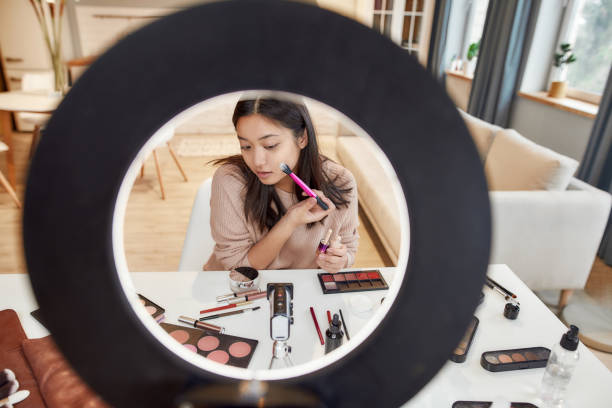 istock Beauty Enhancement. Asian female blogger applying makeup while recording a tutorial video for her beauty blog using camera at home 1225453720
