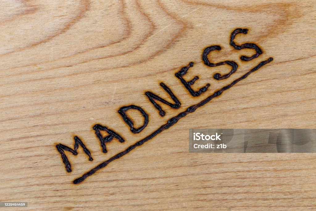 the word madness handwritten with woodburner on flat plywood surface in flat lay directly above view with diagonal composition the word madness handwritten with woodburner on flat plywood surface in flat lay directly above view with diagonal composition. Monday Stock Photo