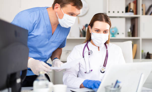 istock Doctor and nurse in protective mask check patient data in hospital computer database 1225455959