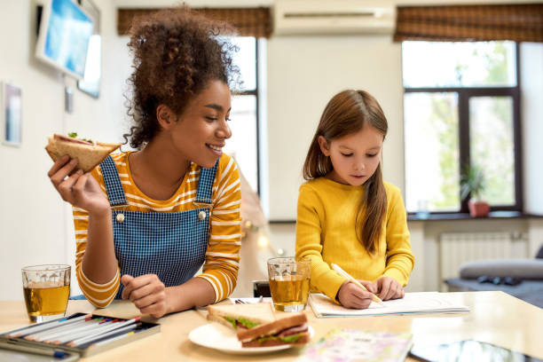 Always there for baby care. African american woman baby sitter entertaining caucasian cute little girl. Kid is drawing while having lunch with her nanny. Leisure activities, babysitting concept African american woman baby sitter entertaining caucasian cute little girl. Kid is drawing while having lunch with her nanny. Leisure activities, babysitting concept. Horizontal shot nanny stock pictures, royalty-free photos & images