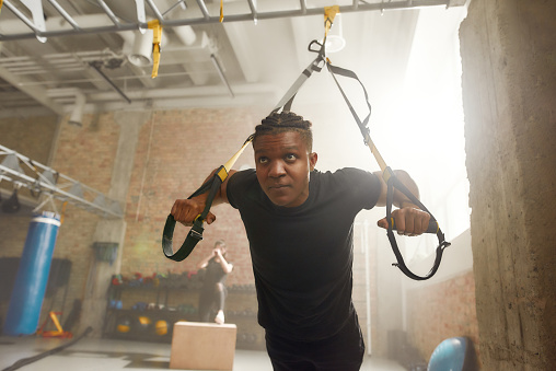 Athletic young man doing fitness training exercises at industrial gym. Push-up, group workout concept. Horizontal shot. Selective focus