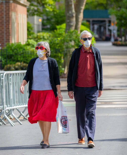 Senior couple wearing N95 face mask walking in Manhattan, New York City Manhattan, New York, USA - May 16, 2020: Senior couple wearing N95 face mask walking through the Washington Square Park entrance on a warm spring day in New York City. person wearing n95 mask stock pictures, royalty-free photos & images