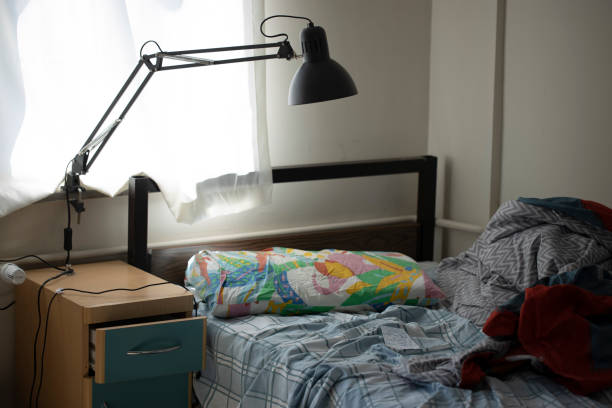 Untidy single bedroom. Alone single man. There is a table lamp by the window.