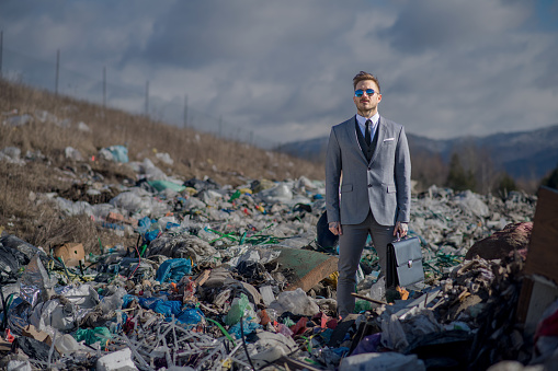 Fashionable modern businessman on landfill, consumerism versus pollution concept.
