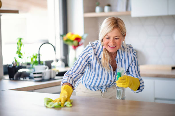 porträt der seniorin reinigung küchentheke drinnen zu hause. - cleaning domestic kitchen counter top housework stock-fotos und bilder