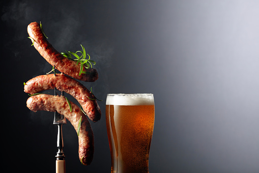 Beer and grilled Bavarian sausages with rosemary. Sausages on a fork sprinkled with rosemary. Copy space.
