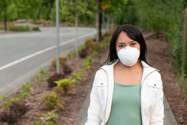 Young hispanic woman wearing N95 face mask while walking on the street Young latina woman wearing N95 face mask while walking on the street. Safe from coronavirus. person wearing n95 mask stock pictures, royalty-free photos & images