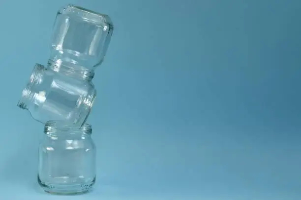 Photo of Vertical row of crooked glass jars on top of each other on a blue background, on the left closeup.