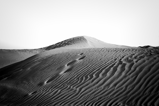 A black and white imagery of a Desert sand with foot steps with waves and textures.