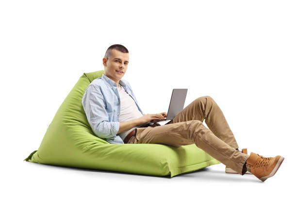 istock Guy with a laptop sitting on a green bean bag and looking at the camera 1225484528