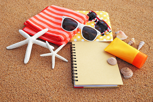 Summer on the beach concept. Arranged the towels, sunglasses, sunscreen and notebooks on the sandy beach, decorated with starfish and shells in the summer sun.
