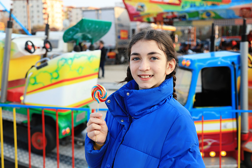 Happy young girl eating a lollypop in amusement park