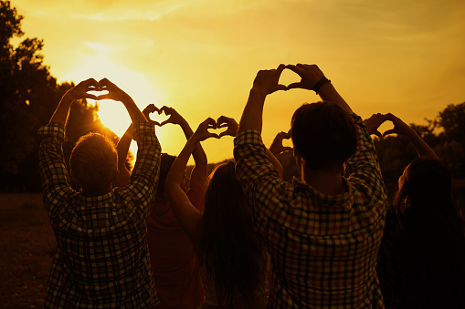 A heart made by the hands of a group of people on a sunset evening background.