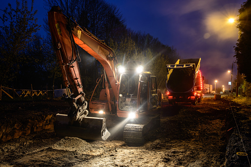 Orange excavator digger working at night on the street lights