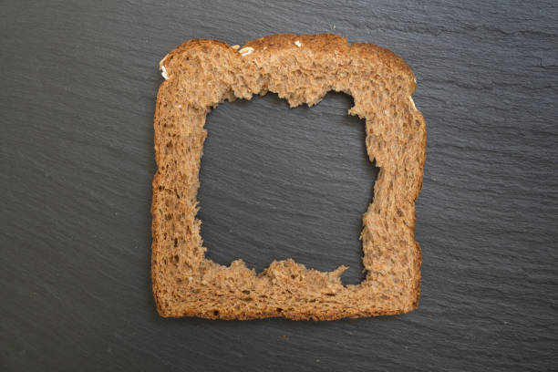 Whole grain sandwich bread slice with hole, on dark surface/ background.
