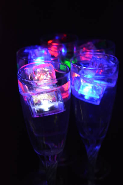 cinco taças de vidro em uma longa perna torcida com cubos de gelo brilhando em cores diferentes. bebidas divertidas e brilhantes com elementos luminosos com led estão localizadas em um fundo preto fosco, festa e relaxamento. - patinagem no gelo - fotografias e filmes do acervo