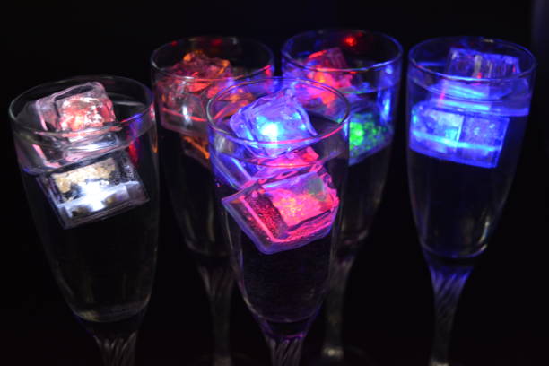 istock Five glass goblets on a long twisted legs with ice cubes glowing in different colors. Fun and bright drinks with luminous led elements are located on a black matte background, party and relaxation. 1225514459