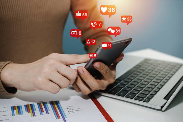 istock hand using social network on digital mobile phone with virtual icon, laptop computer and report on desk at home office, digital marketing, work from home, business finance, network technology concept 1225514612