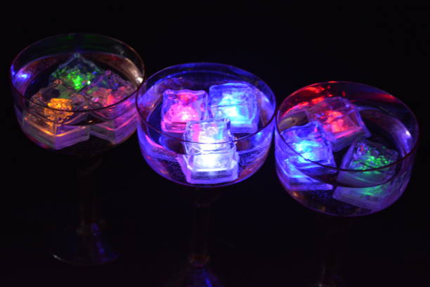 istock Three open champagne glasses with luminous multicolor ice cubes are located on a black matte background. 1225514829