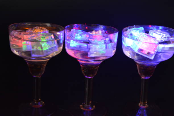 istock Three open champagne glasses with luminous multicolor ice cubes are located on a black matte background. 1225515054