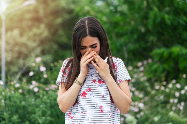 Young pretty woman sneezing in front of blooming tree. Spring allergy concept. Seasonal allergies and health problems. Sinus ache causing very paintful headache. Flu cold symptom. Sinus pain joven mujer bonita estornudando frente al árbol en flor. concepto de alergia a la primavera. alergias estacionales y problemas de salud. dolor de seno causando dolor de cabeza muy pintuosa. síntoma de resfriado de combustión. dolor sinusal