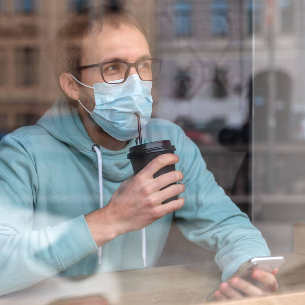istock Man Wearing Mask Drinking Coffee In Cafe Seen Through Window 1225519171